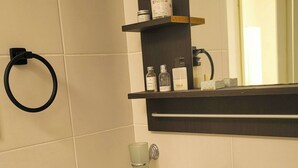 Een badkamer met een witte wasbak, een zwarte kraan en een spiegel erboven. Er zijn planken met toiletartikelen en een handdoekhouder aan de muur.
