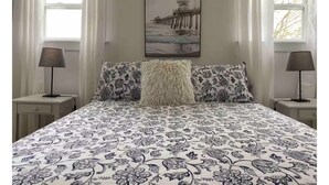 A bedroom with a bed featuring a floral-patterned bedspread, two bedside lamps, a fluffy white throw pillow, and a framed picture of a pier on the wall. - Spacious Country Home 10 minutes from Cavendish (Lot 20)