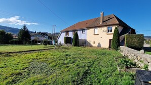 A residential house with a sloped roof, a fenced yard, and a stone wall. - The House of Mountains (Le Thillot)