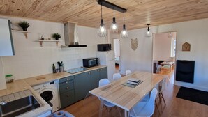 A modern kitchen with wooden cabinets, a built-in microwave, and a dining area with a table and chairs. - The House of Mountains (Le Thillot)