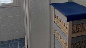 Une pièce dotée d’une porte coulissante, d’une fenêtre avec un rideau et d’une étagère en osier dont le dessus est bleu.