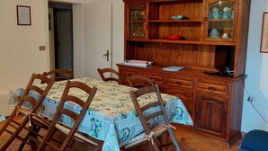 Un coin repas avec une table dressée pour quatre personnes, entourée de chaises en bois. Un buffet en bois, doté de portes en verre, est adossé au mur, et un canapé bleu se trouve au premier plan.
