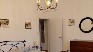 Une chambre à coucher avec un lit, deux chaises, une commode, un lustre et des tableaux encadrés accrochés au mur.