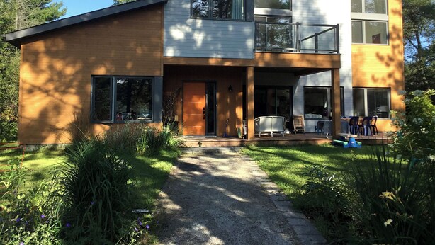 Ein modernes, zweistöckiges Haus mit überdachter Veranda, großen Fenstern und einem gepflegten Garten.