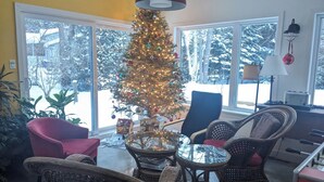 Ein gemütliches Wohnzimmer mit Korbmöbeln, einem Weihnachtsbaum und großen Fenstern mit Blick auf Schnee.