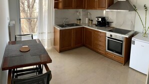 A compact kitchen with wooden cabinets, a built-in oven, a coffee maker, and a small refrigerator. - The Temple of Comfort (Athina)