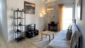 A modern living room with a sofa, TV, bookshelf, and desk. - The Temple of Comfort (Athina)