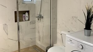 A modern bathroom with a glass-enclosed shower, a toilet, and a washing machine. - The Temple of Comfort (Athina)