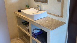 Une salle de bain avec un lavabo blanc, un miroir et une étagère contenant des articles de toilette.
