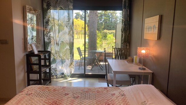 Une chambre à coucher avec un lit, un bureau, une chaise et une table. Il y a une fenêtre avec des rideaux, un cadre photo accroché au mur et une lampe sur la table.