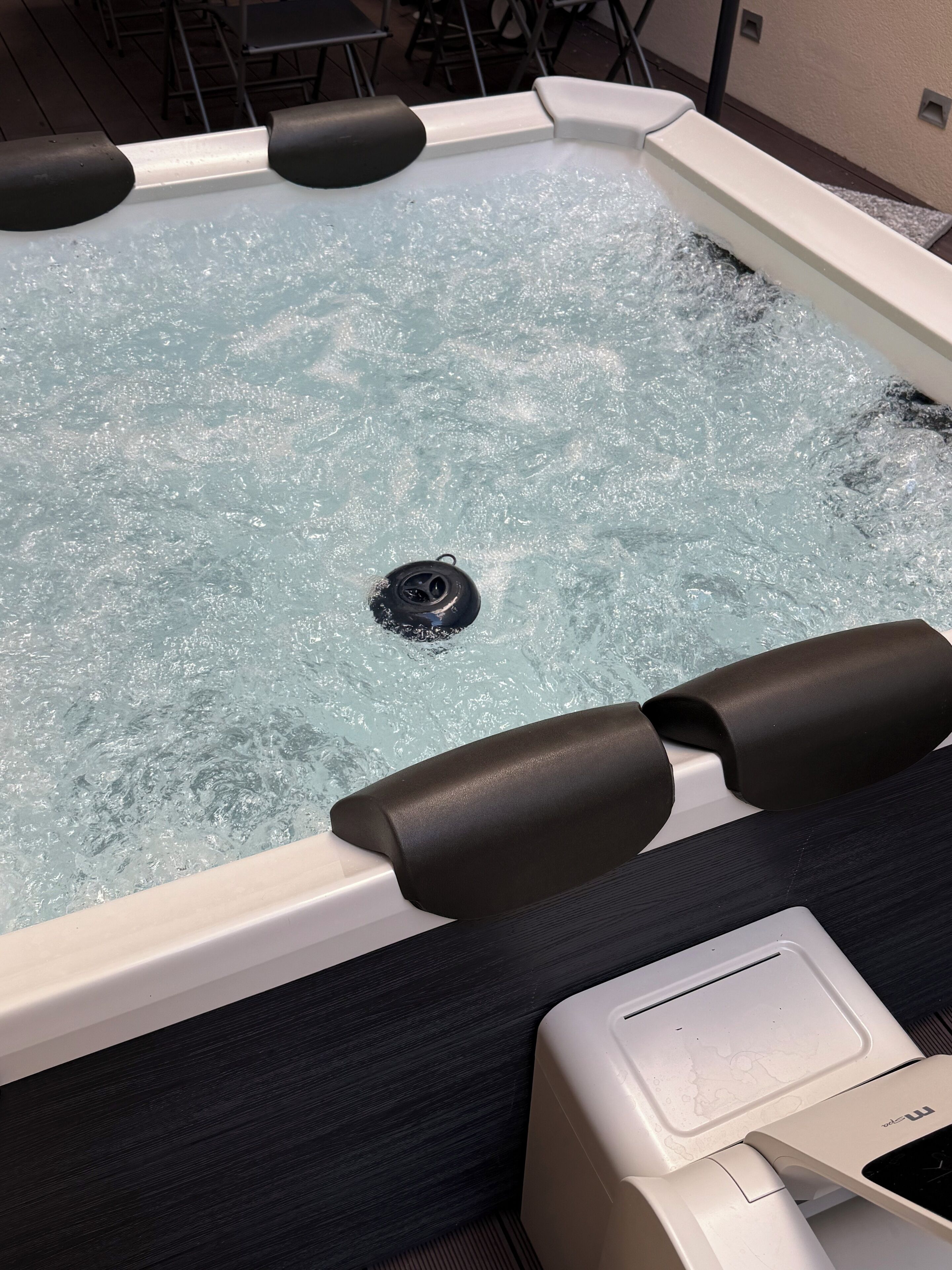 A hot tub with a drain in the center, surrounded by black foam edges, and a white control panel on the side.