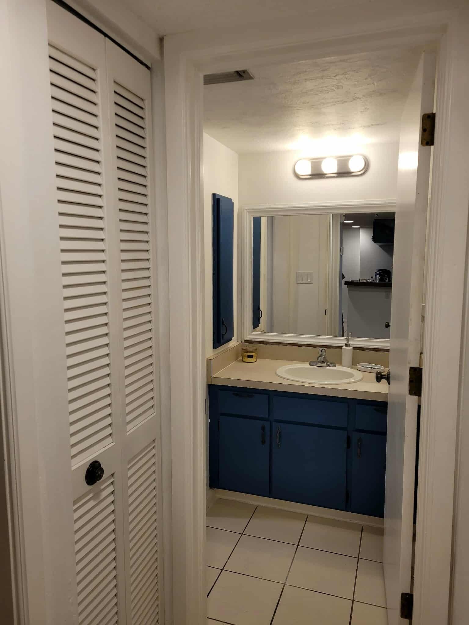 Une salle de bain avec un sol carrelé de carreaux blancs, un lavabo, un miroir et des meubles bleus.