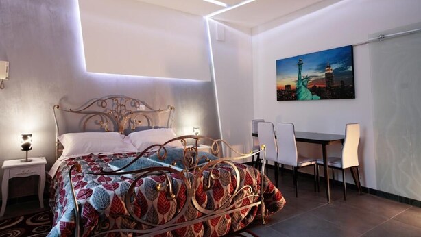 A modern bedroom with a bed, bedside table, and a desk with chairs. - Harmony Living-Theatro Massimo Studio- City Center (Catania)
