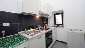 A compact kitchen with a gas stove, sink, and oven. There is a window with a view of the outside, and a small refrigerator. - Harmony Living-Theatro Massimo Studio- City Center (Catania)
