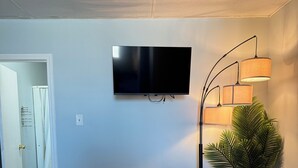 Un soggiorno con una TV a schermo piatto, un tavolino da caffè in legno scuro, un divano, una lampada da terra e una pianta in vaso.