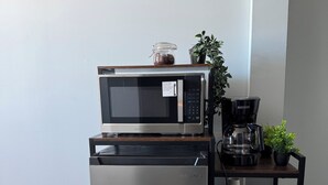 Un angolo cottura compatto con un frigorifero in acciaio inox, un forno a microonde e una moka su un ripiano in legno.