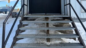 Una scala in metallo conduce a un edificio con una porta nera e un piccolo portico.
