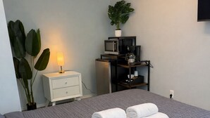 Un letto rifatto con cura, asciugamani arrotolati, un comodino con una lampada, una piccola pianta e un forno a microonde su uno scaffale.