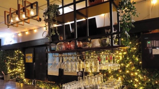 Zona bar con un bancone, scaffali con bicchieri e luci decorative.