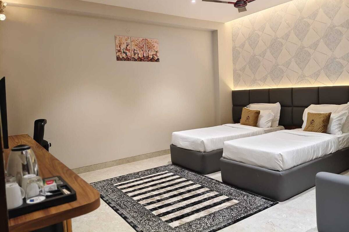 Ein Hotelzimmer mit zwei Betten, einem Schreibtisch mit Kaffeezubereitungsmöglichkeiten, einem Deckenventilator und einem Wandbild.