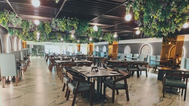 A spacious dining area with multiple tables and chairs, a marble floor, and hanging greenery. - THE CROWN TOWN BIDAR (Bidar)