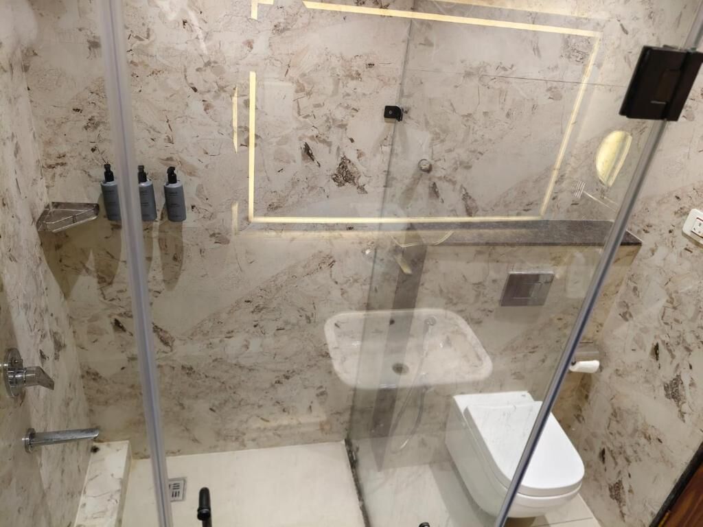 Un baño con ducha de mampara de vidrio, inodoro blanco y pared de mármol.