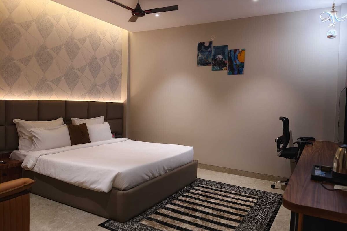 Ein modernes Hotelzimmer mit einem großen Bett, einem Schreibtisch, einem Sessel, einem Deckenventilator und Kunstwerken an den Wänden.