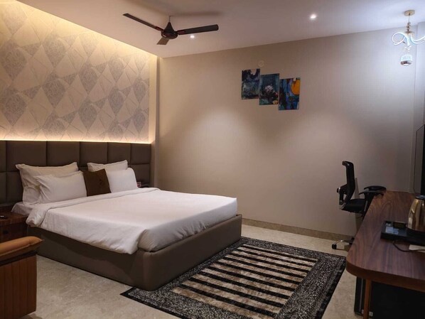 Una habitación de hotel moderna con una cama grande, un escritorio, una silla, un ventilador de techo y obras de arte en las paredes.