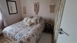 A bedroom with a bed, a bedside table, a chair, and a window with curtains. - Single-storey seaside house (Santec)