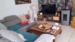 A living room with a sofa, coffee table, TV, and a fireplace. - Single-storey seaside house (Santec)