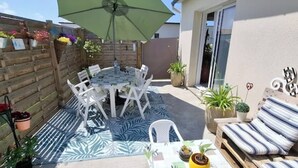 A patio with a round table and chairs, surrounded by potted plants and a striped outdoor rug. - Single-storey seaside house (Santec)