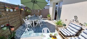 Eine Terrasse mit rundem Tisch und Stühlen, umgeben von Topfpflanzen und einer gestreiften Outdoor-Isolde.