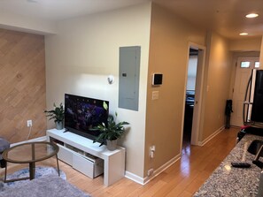 A living room with a TV, two potted plants, a glass coffee table, and a white entertainment unit.