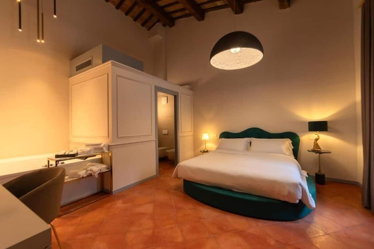 A bedroom with a bed, a desk, a chair, a wardrobe, and a hanging light fixture.