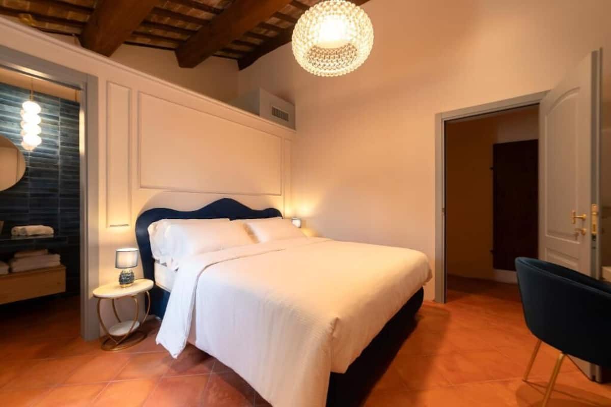 A bedroom with a bed, bedside table, lamp, and a chair.