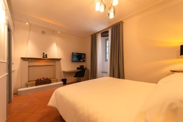 A hotel room with a large bed, a desk with a chair, a television, and a fireplace. - Maison Ventiquattro Suite & Spa (Talamello)