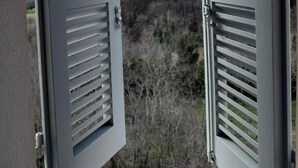 A view through open white shutters with horizontal slats, overlooking a hilly landscape with sparse vegetation and a partly cloudy sky. - Maison Ventiquattro Suite & Spa (Talamello)