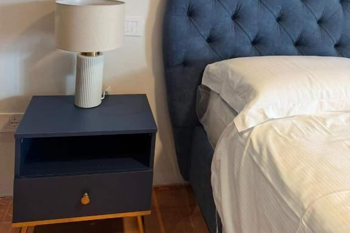 A bedroom with a tufted blue headboard, a bedside table with a lamp, and a bed with white bedding.