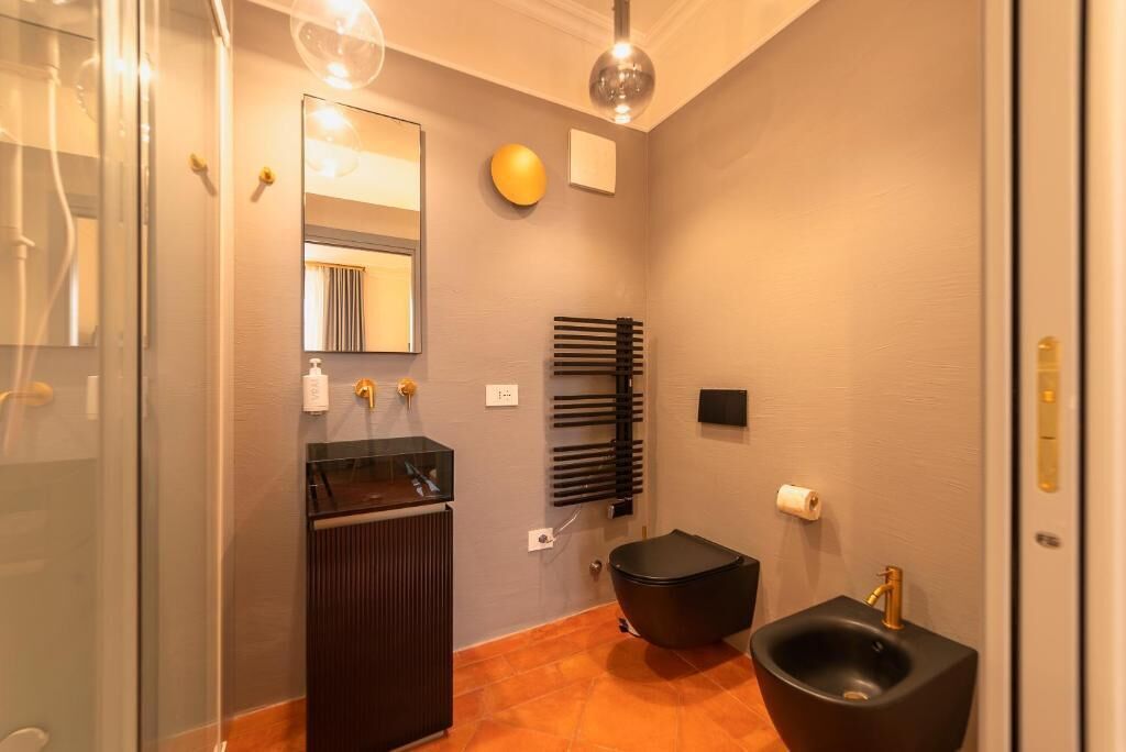 A modern bathroom with a glass shower enclosure, a dark vanity, a black bidet, and a mirror with a light above it.