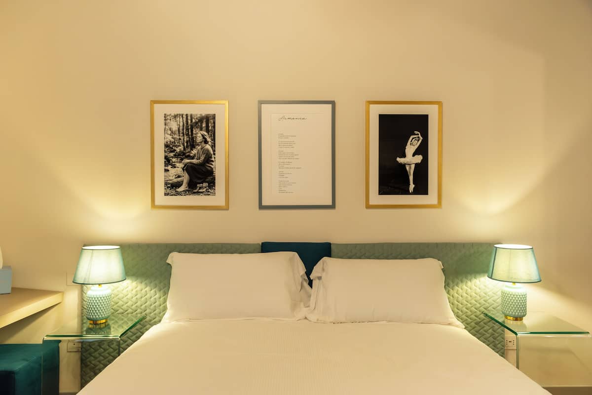 A neatly made bed with white linens, two bedside lamps, and three framed pictures on the wall.