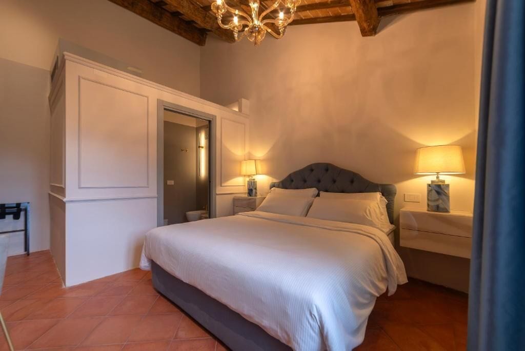 Une chambre à coucher avec un grand lit, deux tables de chevet avec des lampes, une porte et un lustre.