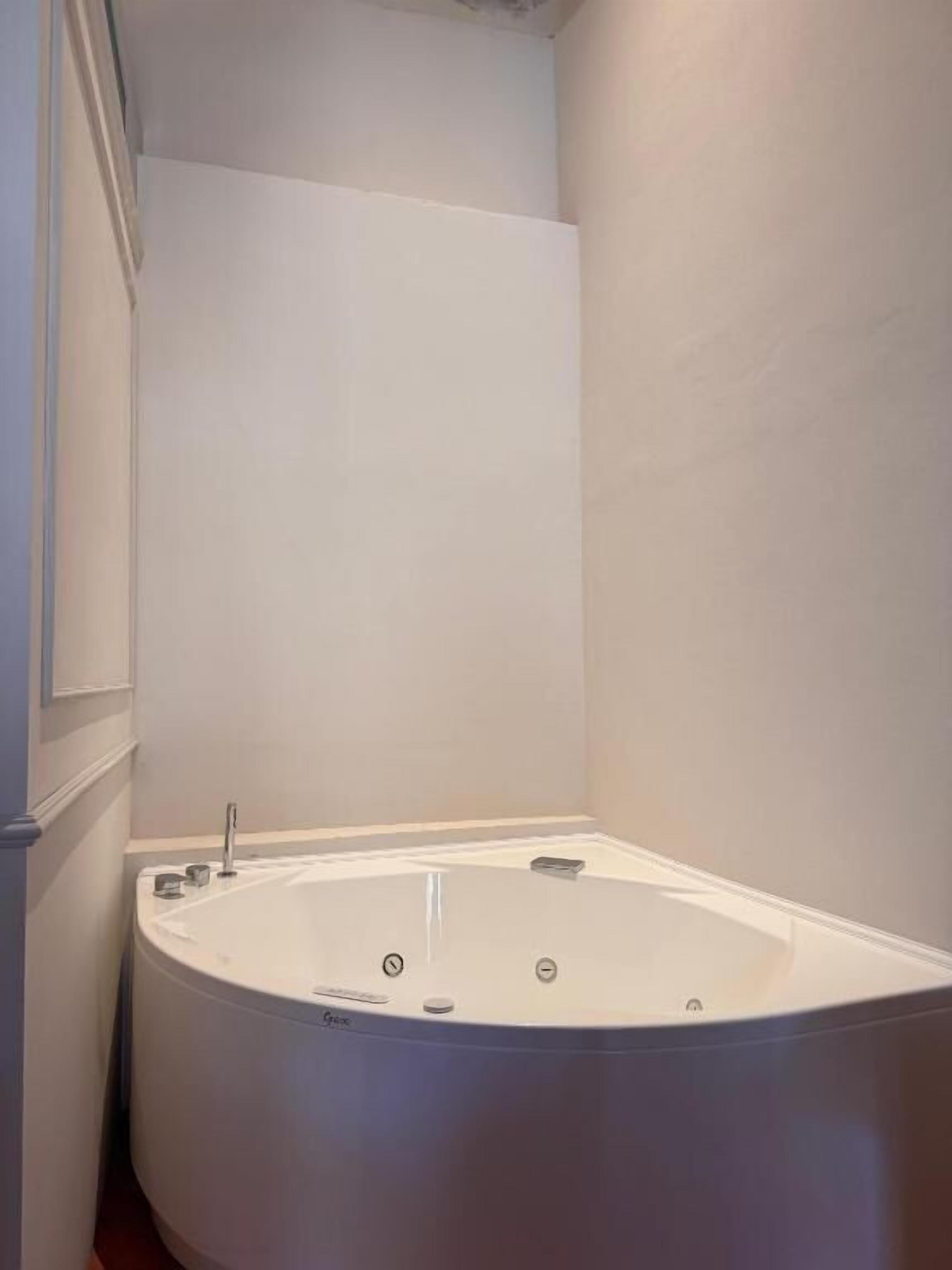 Un baño en esquina con bañera independiente, paredes blancas y zona de ducha visible.