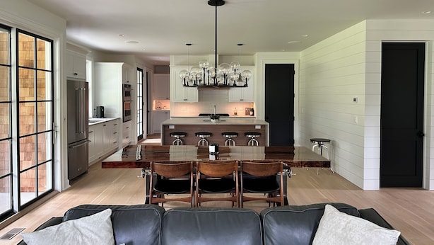 Una cocina moderna con una isla central, taburetes de bar y una zona de comedor con un sofá de cuero negro.