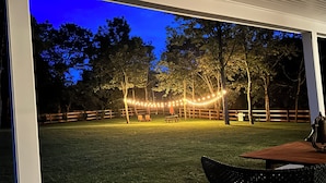 Un patio al aire libre con valla de madera, luces colgantes y una mesa con sillas.