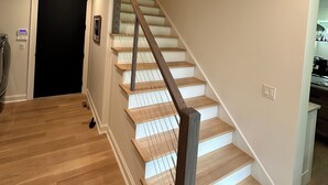 Una escalera de madera con escalones y barandilla, que lleva a un rellano con una puerta negra y un interruptor de luz.