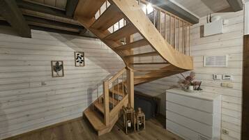 Un escalier en colimaçon en bois se trouve dans une pièce aux murs en bois peints en blanc, avec une armoire blanche et des tableaux encadrés.
