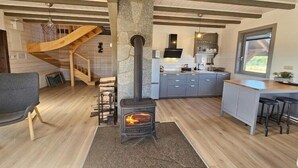A modern kitchen with a central wood-burning stove, a grey countertop, and a wooden staircase. - Comfortable holiday home with a terrace and garden (Borsk)