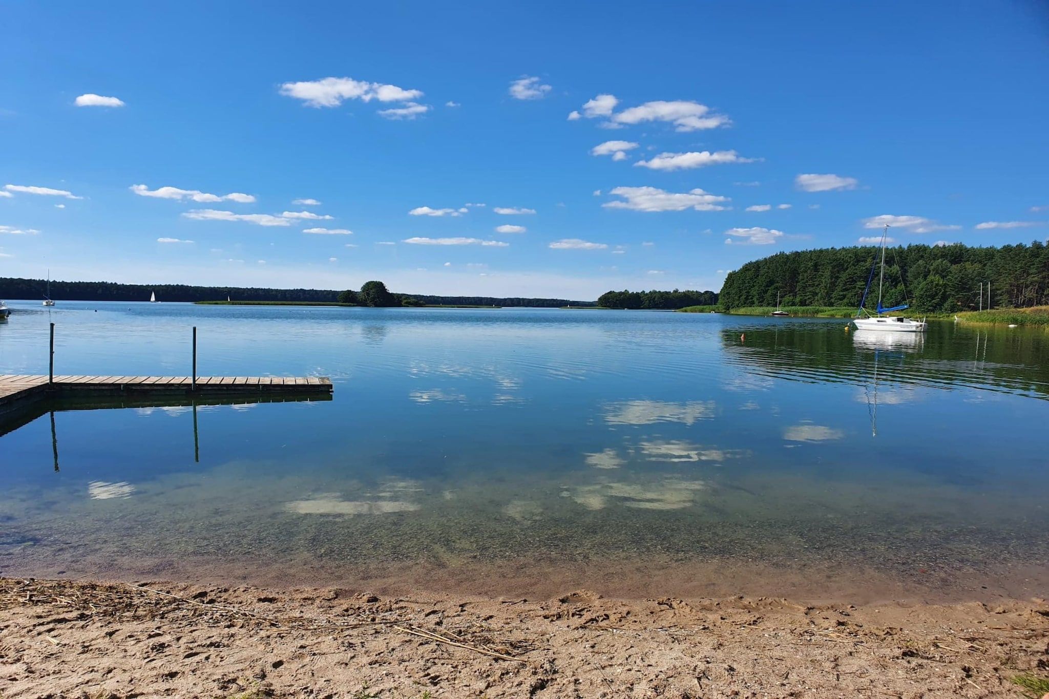 Un lac paisible avec une jetée en bois qui s’avance sur l’eau, entouré de terres boisées.