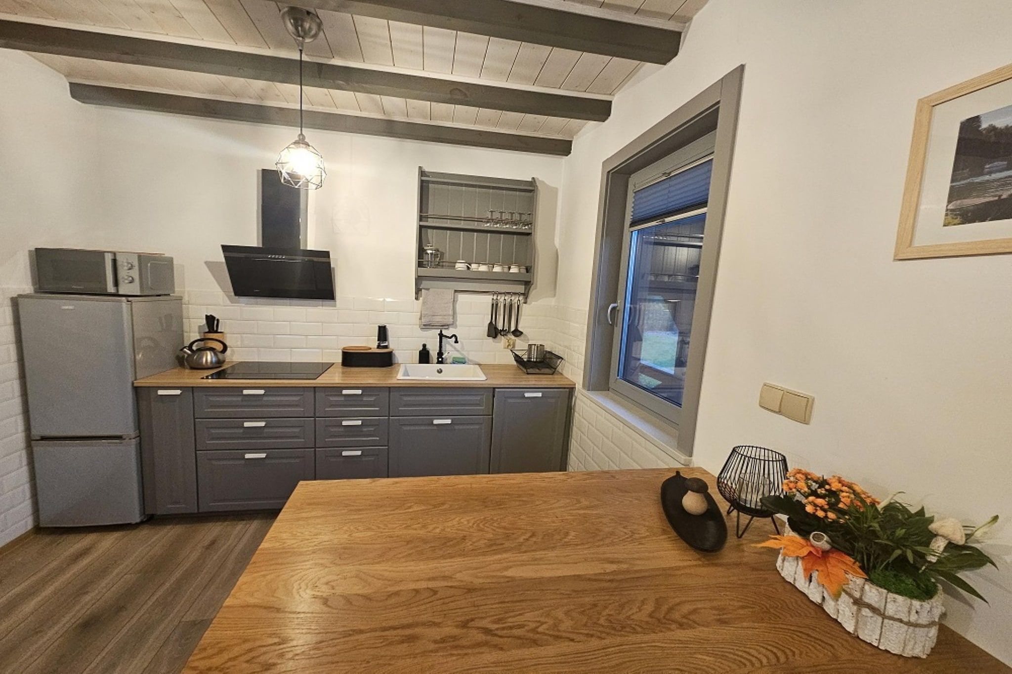 Een moderne keuken met grijze kastjes, een houten eettafel en een raam met uitzicht.