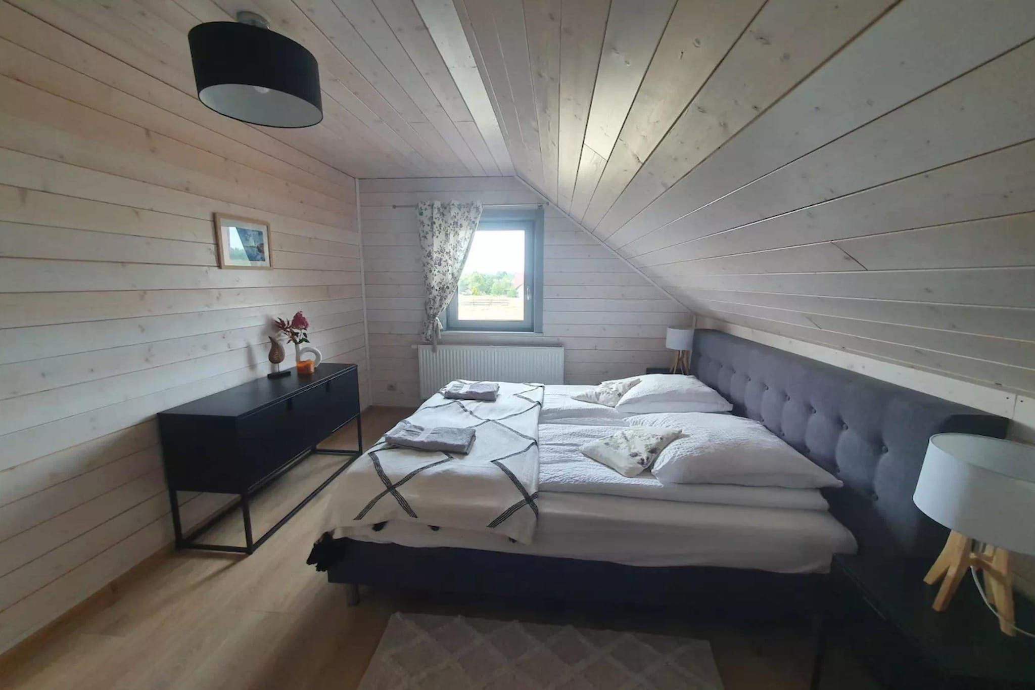 Een slaapkamer met een bed, een dressoir, een raam en een lamp.